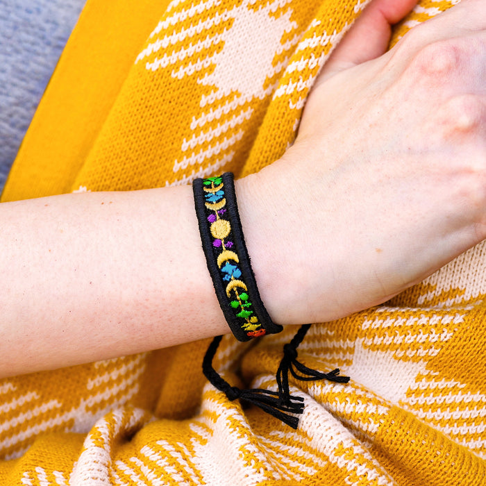 Hand wearing a colorful machine embroidered bracelet on a yellow and white patterned fabric background