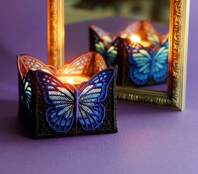 Butterfly-shaped machine embroidered candle holder with lit candles on a purple surface