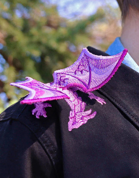Purple dragon machine embroidered patch on a black jacket with blurred greenery in the background