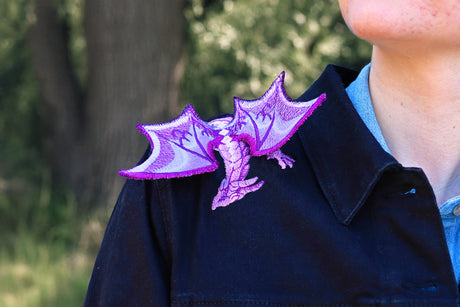 Person wearing a dark jacket with purple 3D dragon design on the shoulders, outdoors.