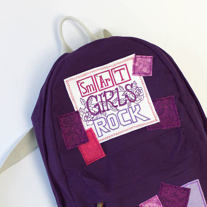 Purple backpack with a machine embroidered patch that says 'Smart Girls Rock' on a white background
