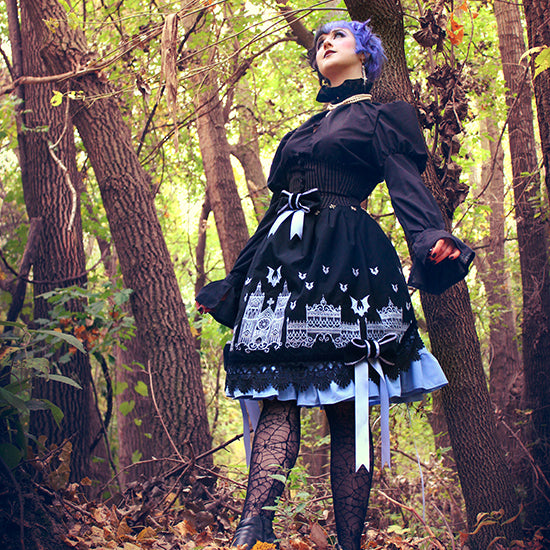 Person standing in a forest in a black dress with machine embroidered Halloween border on the bottom.
