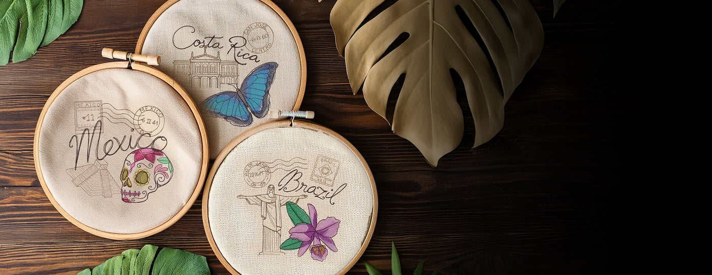 Three embroidery hoops with machine embroidery stamp designs of a Costa Rica, Mexico and Brazil wooden surface with leaves.