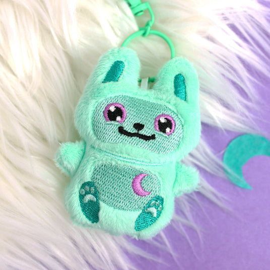 Mint green machine embroidery bunny plush on a keychain on a fluffy white and purple background