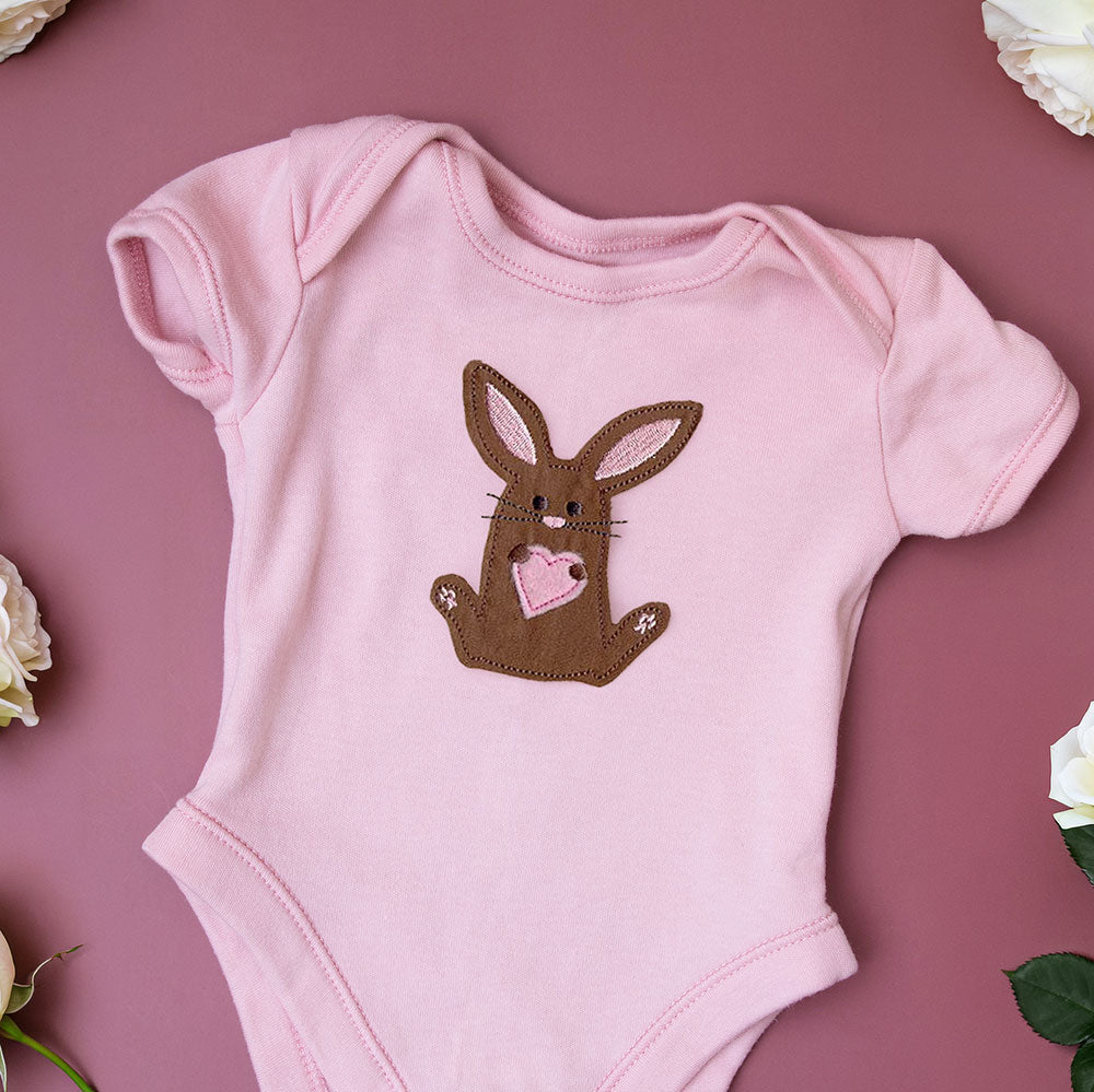Chocolate bunny applique with a pink heart, surrounded by white embroidered flowers on a pink background.