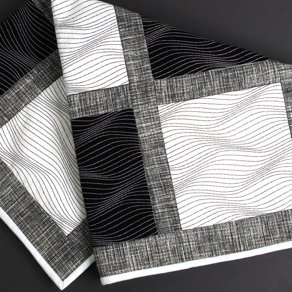 Machine embroidered optical illusion design on black and white fabric on a dark background.