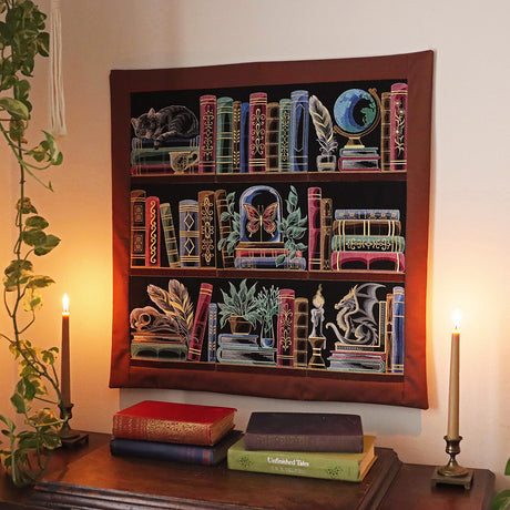 Machine embroidered wall hanging featuring bookshelf themed designs on a wall above a table with books and candles.