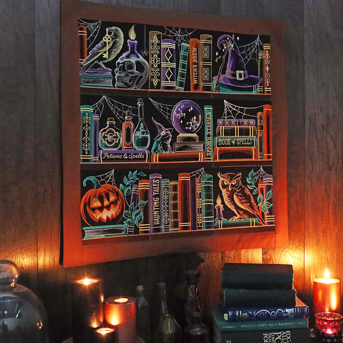 Decorative wall hanging featuring Halloween-themed machine embroidery designs including books, pumpkins, and bottles on a wooden wall.