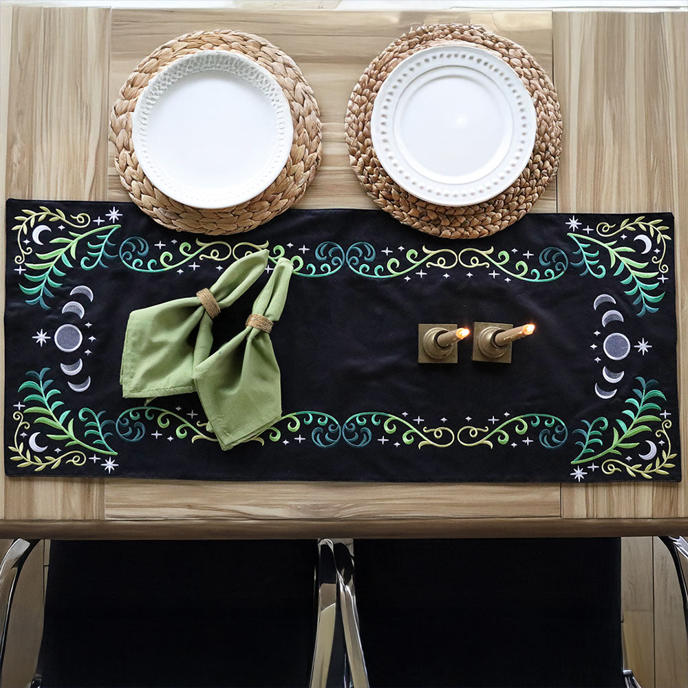 Celestial Flourish Design Pack embroidery decorates green napkins on a wooden table, with candles and two place settings.
