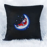 Black square pillow with embroidered design of Santa Claus in red suit lying on a glowing blue crescent moon surrounded by small stars.