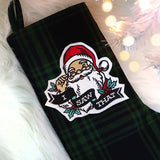 A dark green plaid Christmas stocking features an embroidered patch of Santa winking and holding glasses with the words I SAW THAT on a ribbon.