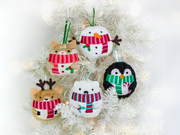Set of four machine embroidered Christmas ornament designs - a snowman, penguin, polar bear, cat and reindeer, each wearing scarf, hanging on a white tree