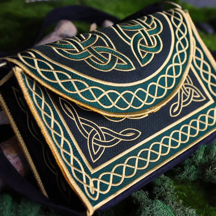 Close up image of a machine embroidered in-the-hoop purse with green and gold Celtic styled motifs stitched onto black fabric.