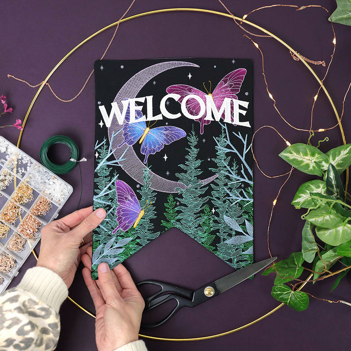 Decorative machine embroidered sign with butterflies and 'WELCOME' text on a purple background with scissors and decorative items.