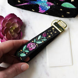 Digitally downloadable machine embroidery design showing pink roses with green leaves and small gold stars on a black wristlet strap.