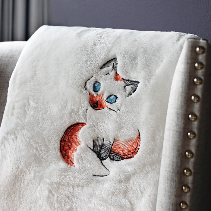 White blanket with embroidered fox design on a gray chair
