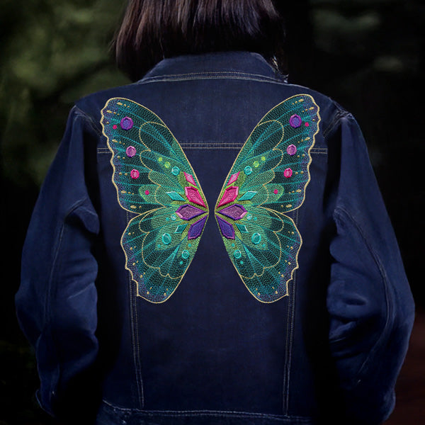 Dark denim jacket with a colorful butterfly wing machine embroidery design on the back against a dark background
