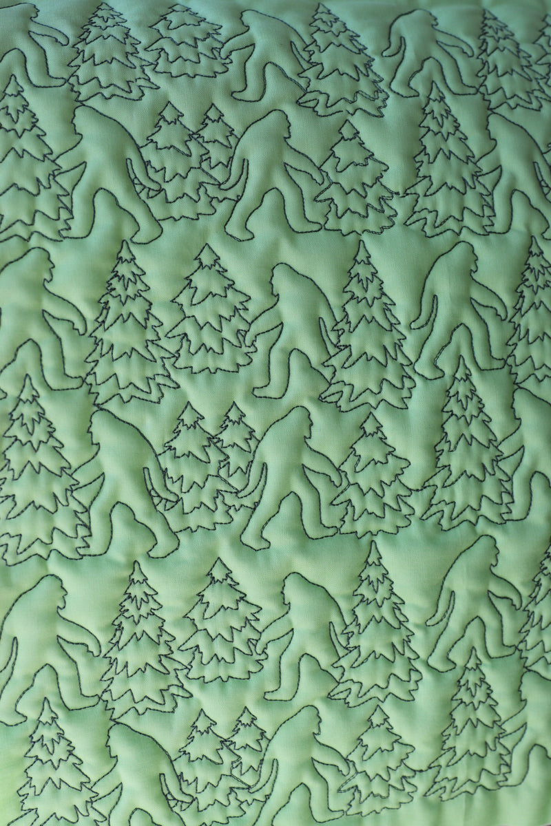 Machine embroidered edge-to-edge quilting sasquatch with trees repeated on green fabric