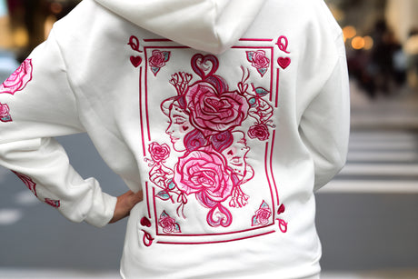 White hoodie with pink floral queen designs on a blurred outdoor background