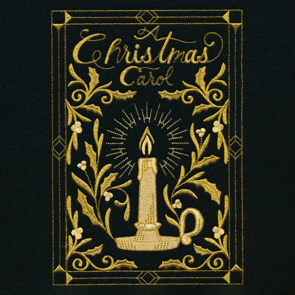 Gold embroidery on black fabric shows a lit candle in a holder surrounded by holly leaves and berries framed by geometric borders above the words "A Christmas Carol.
