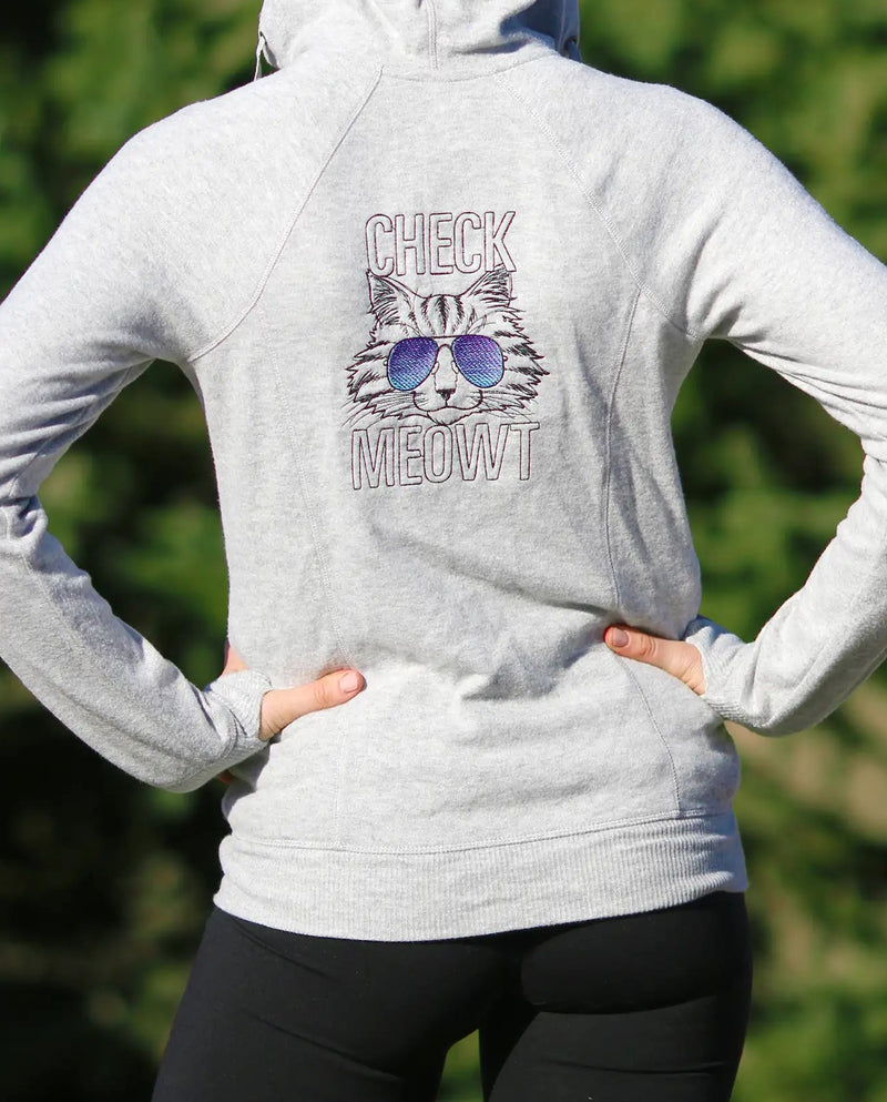 Person wearing a white hoodie with a machine embroidery cat design standing outdoors.
