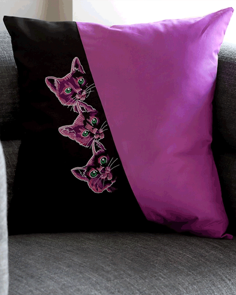 Modern black and purple accent pillow featuring three playful purple cat heads with bright green eyes in machine embroidery, ideal for fun home décor or DIY embroidery projects