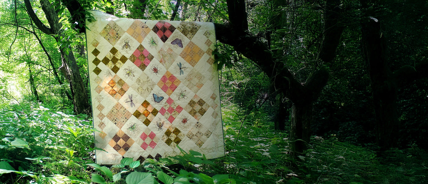 Machine embroidery insect designs on a quilt in a forest setting