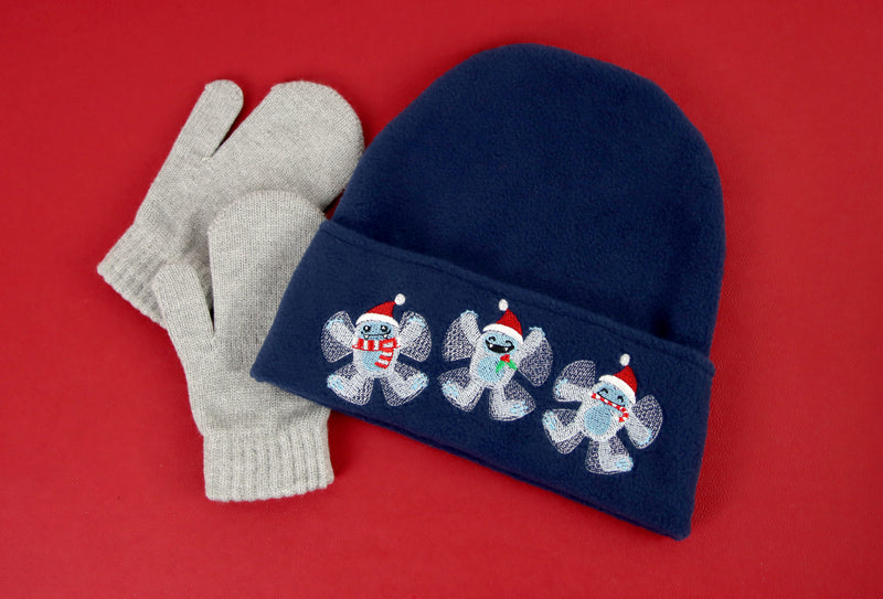 A navy blue winter hat with machine embroidery yeti trio design surrounded by gloves on a red background.