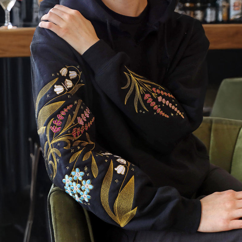 Person wearing a black hoodie with machine embroidery floral design sitting on a green chair.