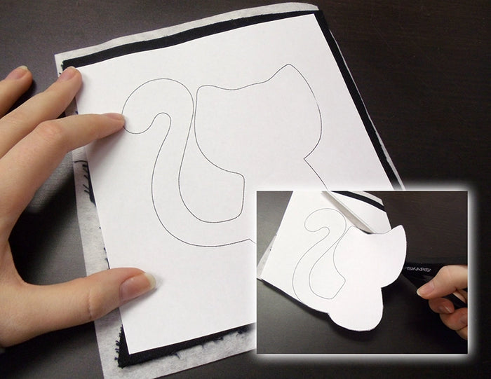 Hand holding a white paper with cut-out template, showing the process of cutting out shapes with a scissors.