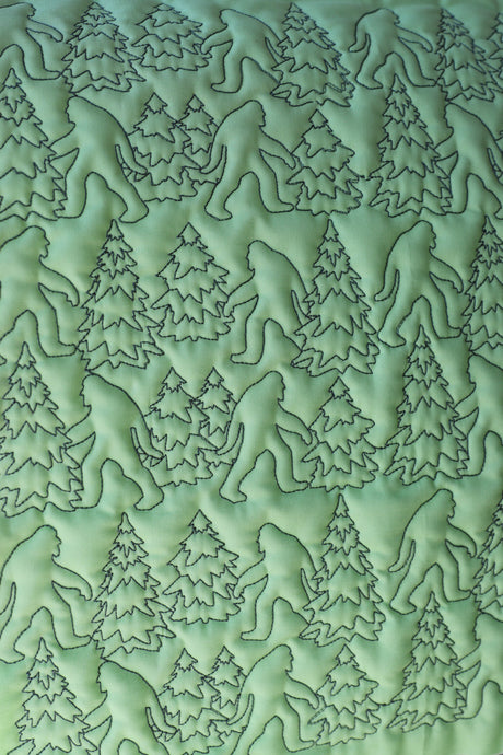 Bigfoot and trees machine embroidery quilting design stitched in dark thread on light green fabric.