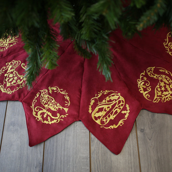 Red Christmas tree skirt with holiday machine embroidery designs underneath a tree