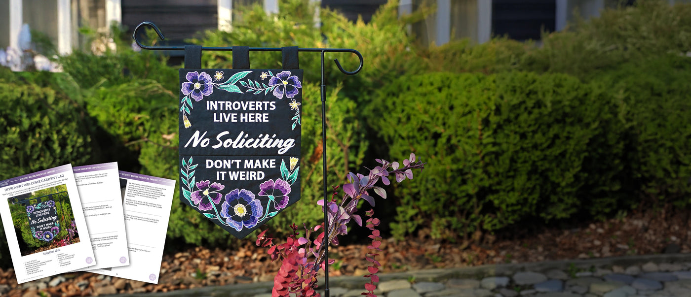 Decorative machine embroidery garden flag with text and flowers in a garden setting, accompanied by printed PDF materials.