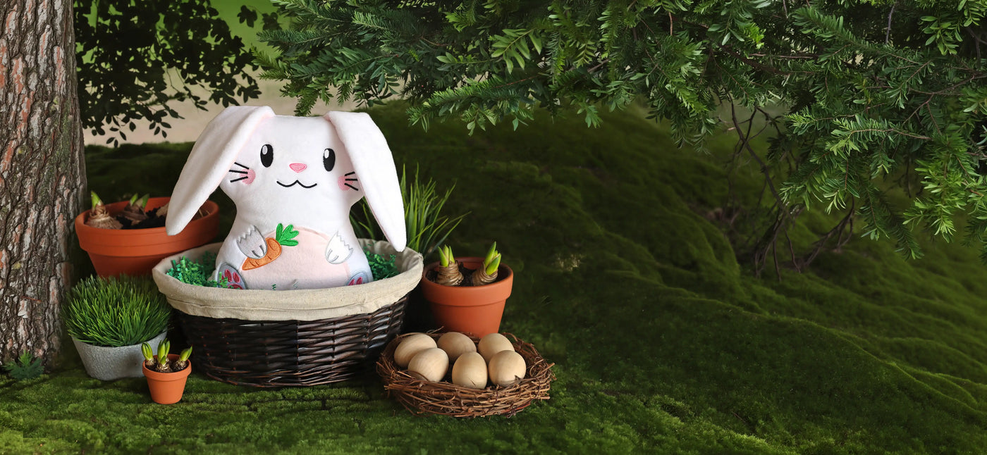 Plush machine embroidery bunny in a basket with Easter eggs and carrots on a green grass background