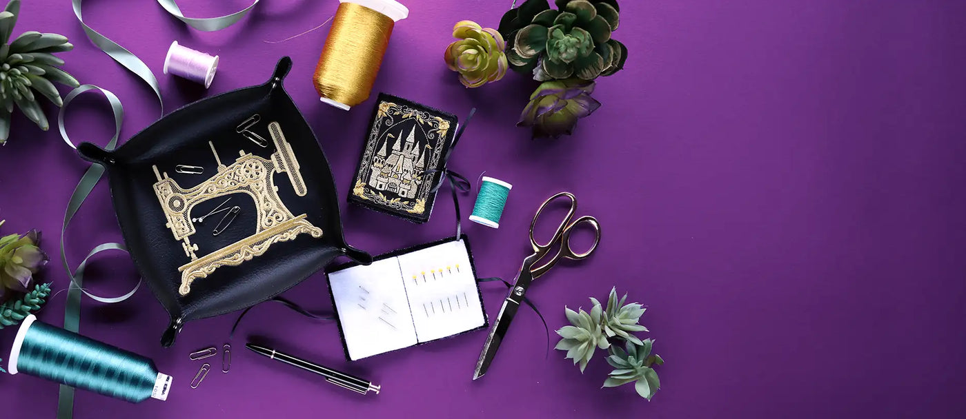 Machine embroidered leather catch all tray and machine embroidered needle staged with scissors and thread on a purple background