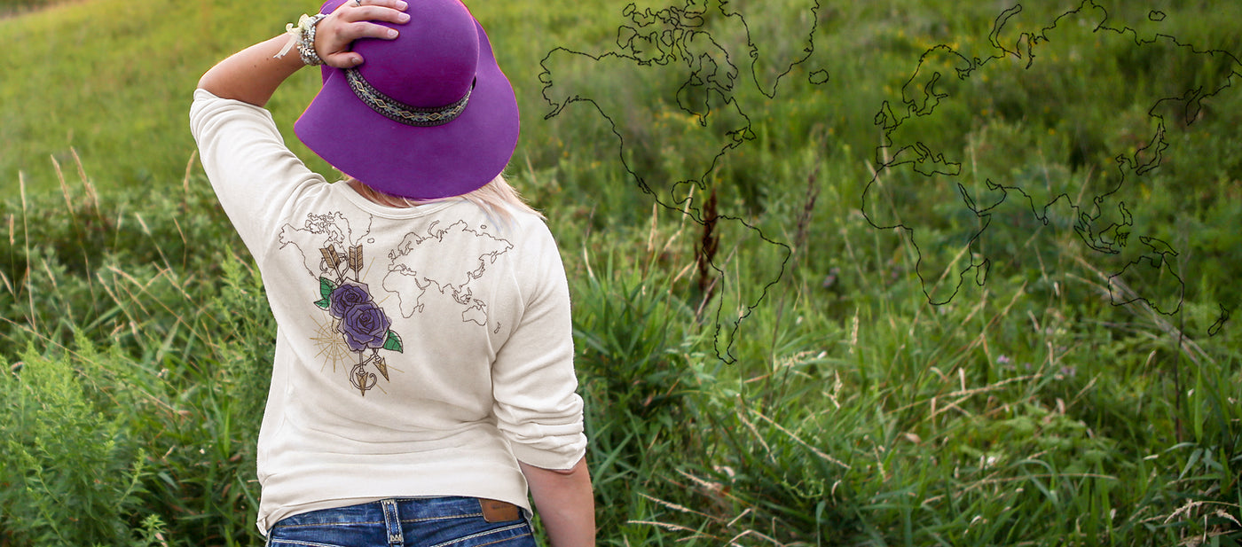 Person wearing a purple hat and white shirt with machine embroidery floral design in a grassy field