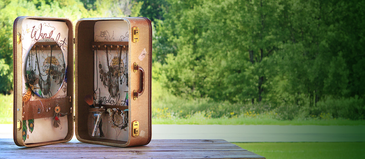 Open suitcase with decorative machine embroidery designs on a wooden surface with a green outdoor background