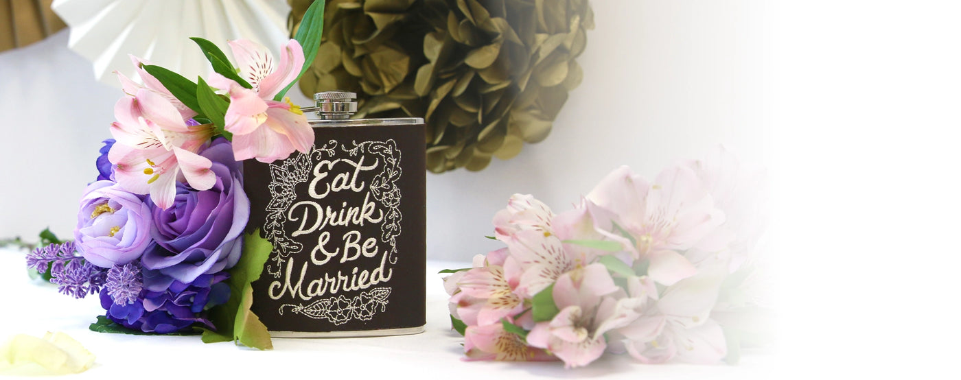Flask with machine embroidered 'Eat, Drink & Be Married' text surrounded by flowers on a white background.