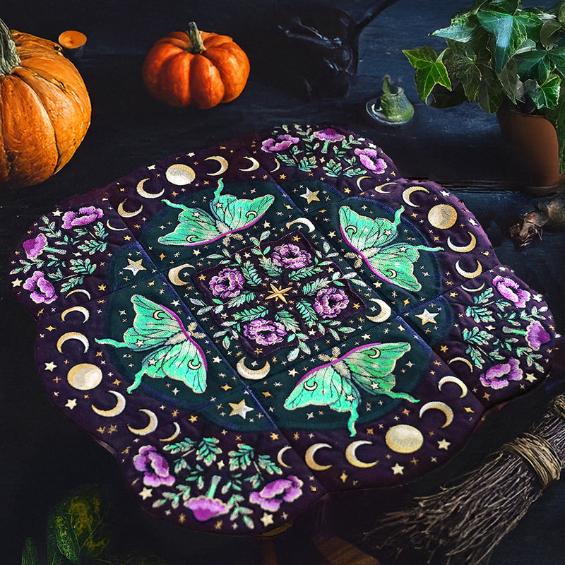 Decorative machine embroidered  mandala table center with butterflies, flowers, and celestial elements on a dark surface with pumpkins and ivy.