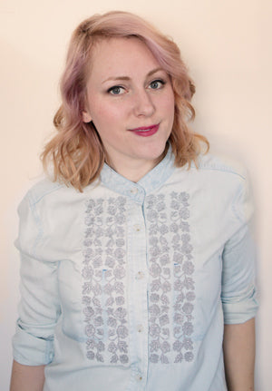 a person wearing a machine embroidery floral design on a denim button up shirt.