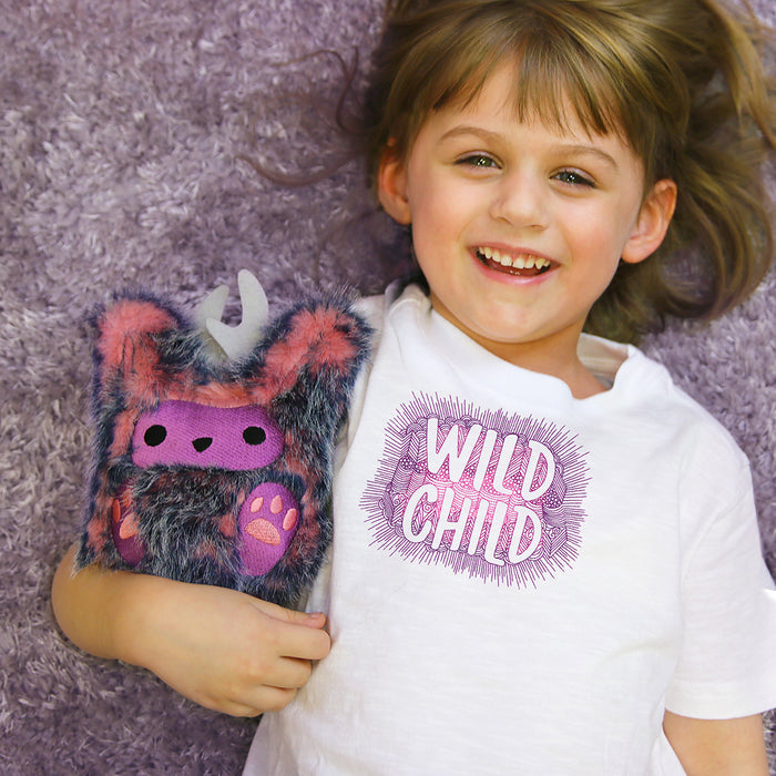 Child wearing 'Wild Child' machine embroidery design on a shirt holding a plush embroidered monster 