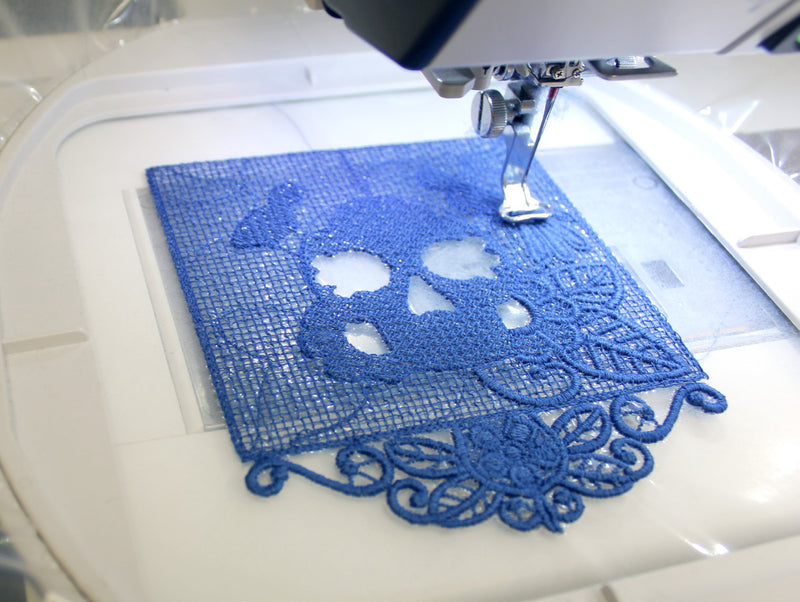 Embroidery machine stitching a blue lace design on fabric.