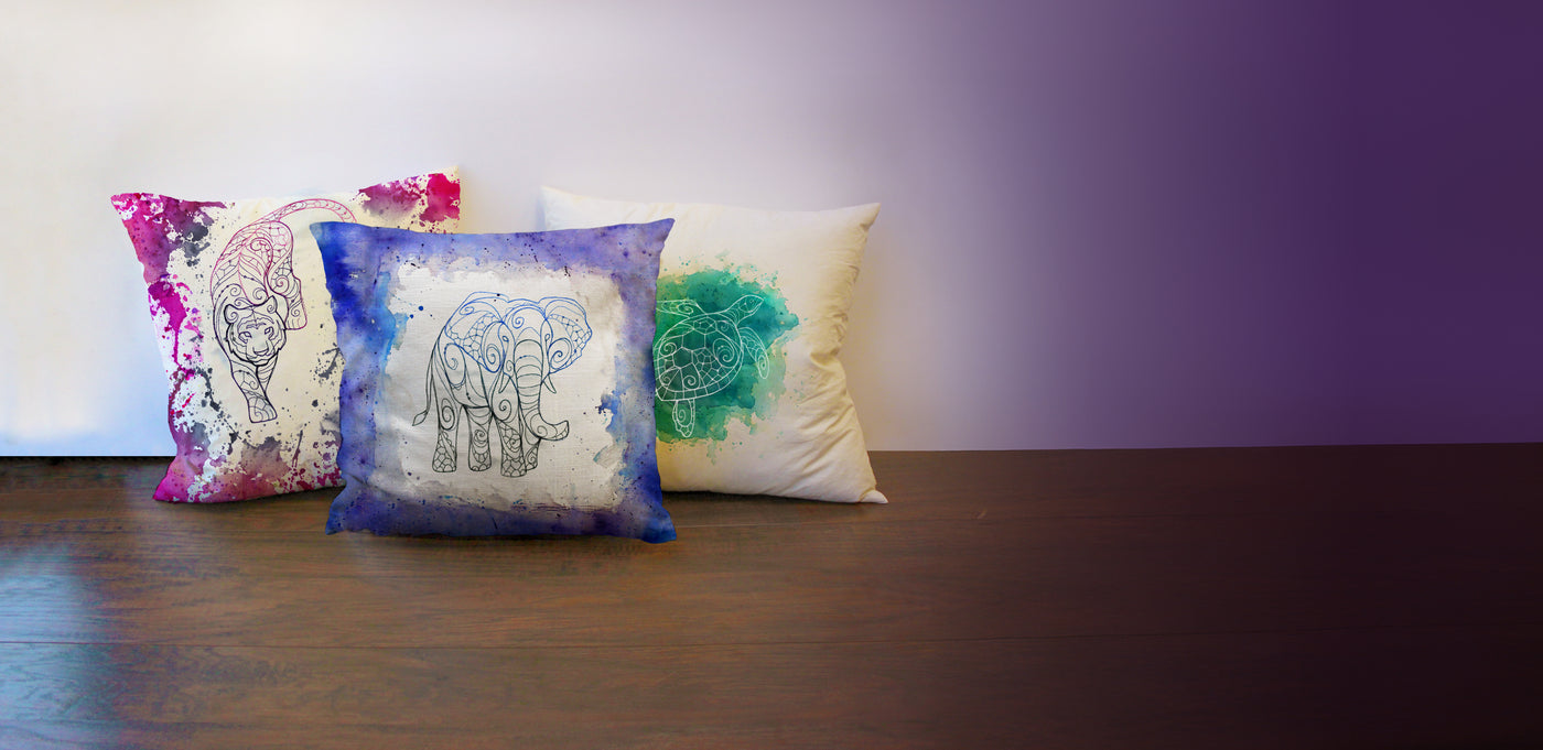 Three decorative pillows with unique designs on a wooden surface against a purple wall.