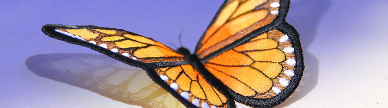 Close-up of a Monarch butterfly machine embroidery design with orange and black patterns on a light purple background